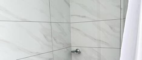 A shower area with white marble tiles, a handheld showerhead, and a wall-mounted faucet.