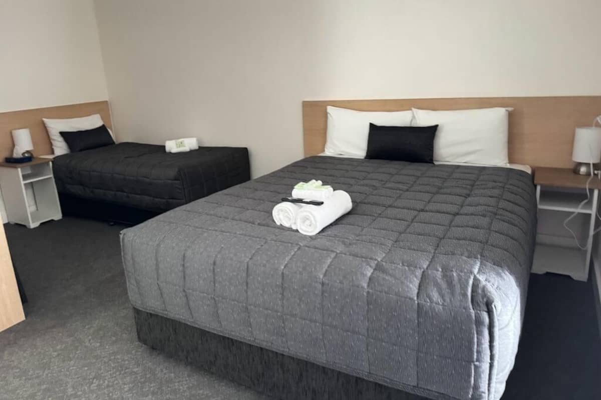 A hotel room with a large bed, a smaller bed, and a nightstand with a lamp.