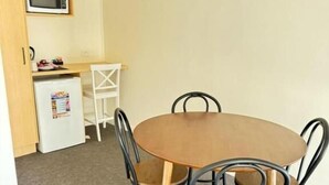 Un comedor pequeño con una mesa redonda y cuatro sillas, un refrigerador compacto, un microondas y una silla blanca al fondo.
