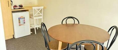 Un comedor pequeño con una mesa redonda y cuatro sillas, un refrigerador compacto, un microondas y una silla blanca al fondo.