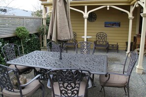 An outdoor patio with a metal table and chairs, surrounded by a yellow wall and a decorative fence.