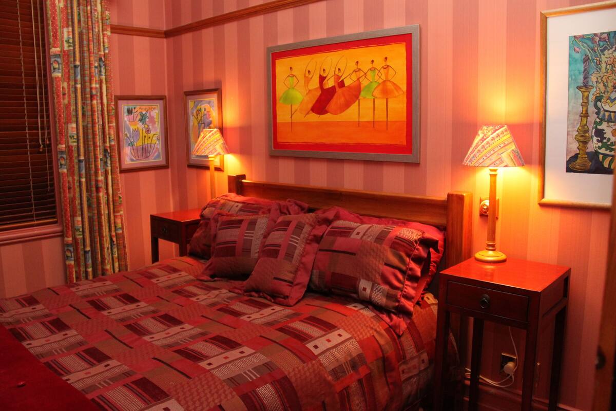 Quarto de hotel com uma cama grande, duas mesas de cabeceira e uma parede com obras de arte emolduradas.