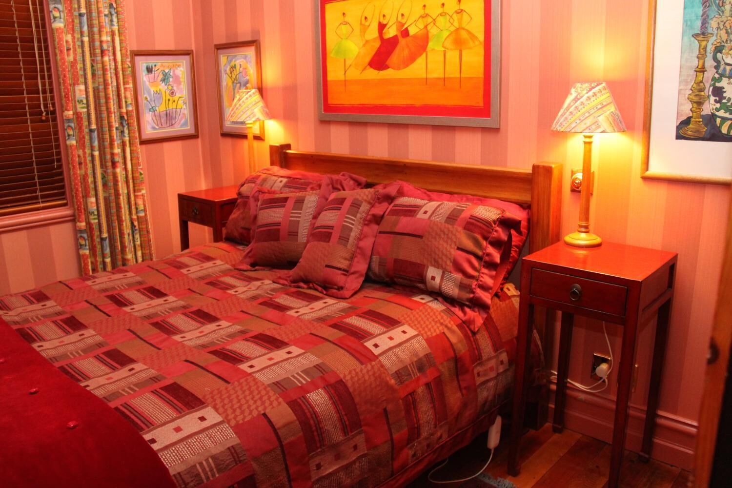 A neatly made bed with a patterned quilt, two bedside lamps, and framed artwork on the walls.