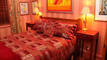 A neatly made bed with a patterned quilt, two bedside lamps, and framed artwork on the walls.