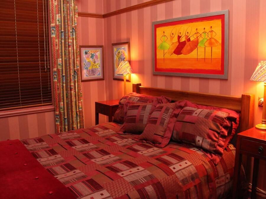 A bedroom with a large bed, striped wallpaper, and two framed artworks on the wall.