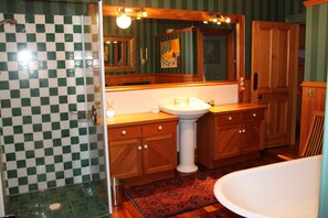 A bathroom with a checkered shower wall, a sink with a pedestal, wooden cabinets, and a large mirror.