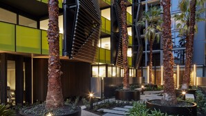 Un edificio moderno con una fachada singular, palmeras y un área exterior bien iluminada con senderos de piedra.