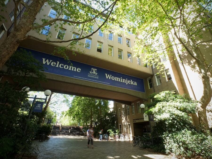 La entrada de un edificio con un letrero que dice 'Welcome' y otro que dice 'Wominkiaka', rodeada de árboles y un camino pavimentado.