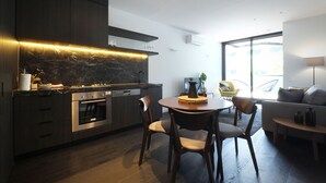 Una cocina moderna con armarios oscuros, horno integrado y un comedor con mesa y sillas redondas.
