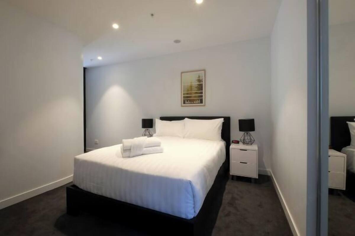 Una habitación de hotel moderna con una cama grande, mesitas de noche y un cuadro enmarcado en la pared.