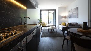 Una cocina moderna con estufa integrada, un comedor con mesa redonda y sillas, y una sala de estar con sofá y lámpara.