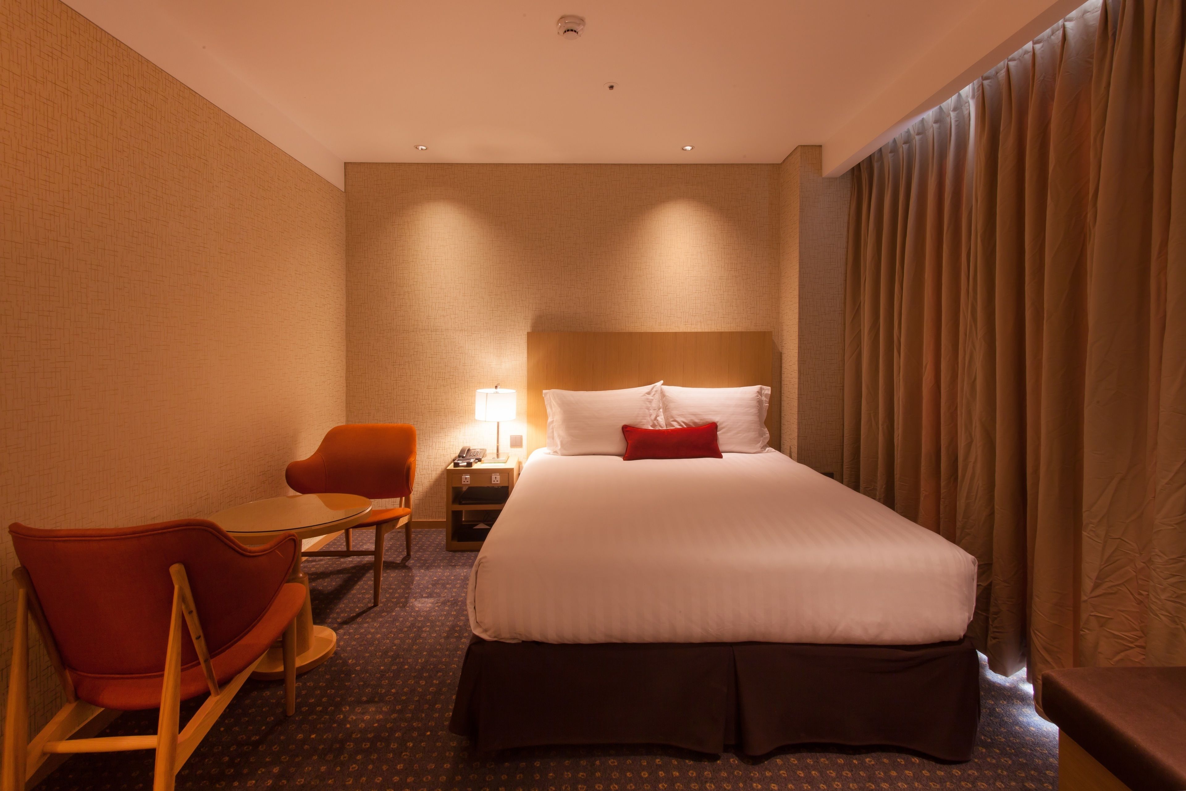 Una habitación de hotel con una cama grande, un escritorio, una silla y una mesita de noche con lámpara.