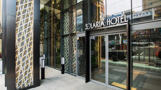 Exterior del Hotel Solaria, con amplias puertas de vidrio y un diseño de fachada geométrica.