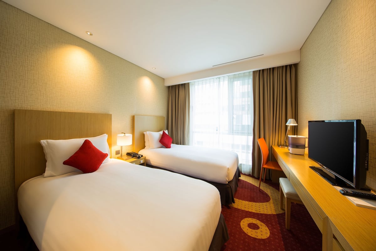 A hotel room with two beds, a desk, a TV, and a window with curtains.