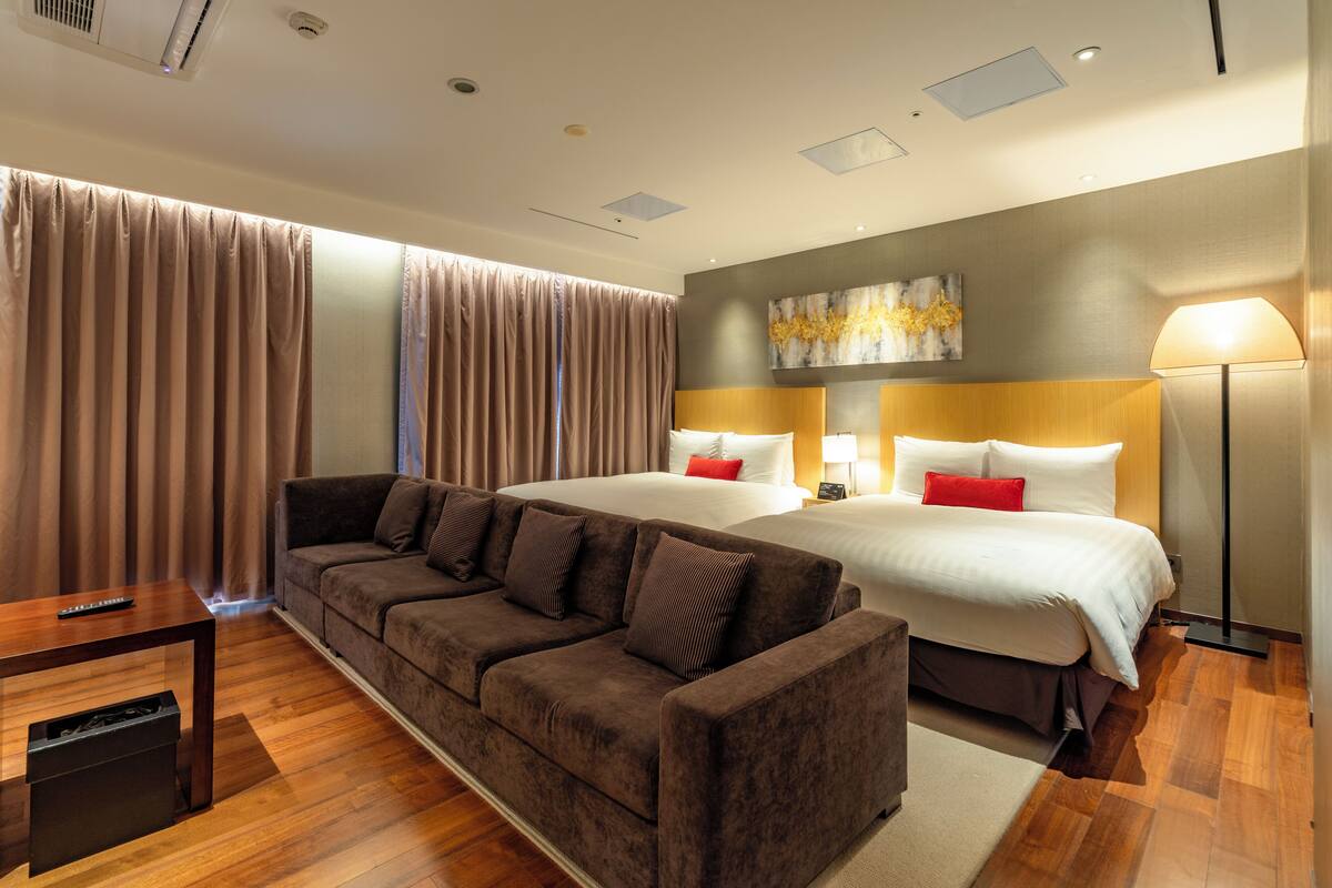 A hotel room with a sofa, a bed, a lamp, and a painting on the wall.