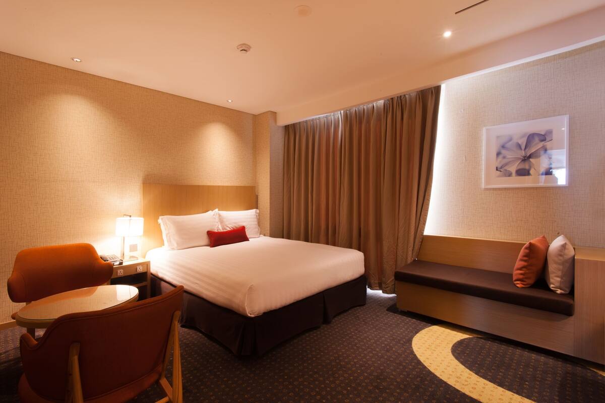 A hotel room with a bed, a desk, a chair, a sofa, and a window with curtains.