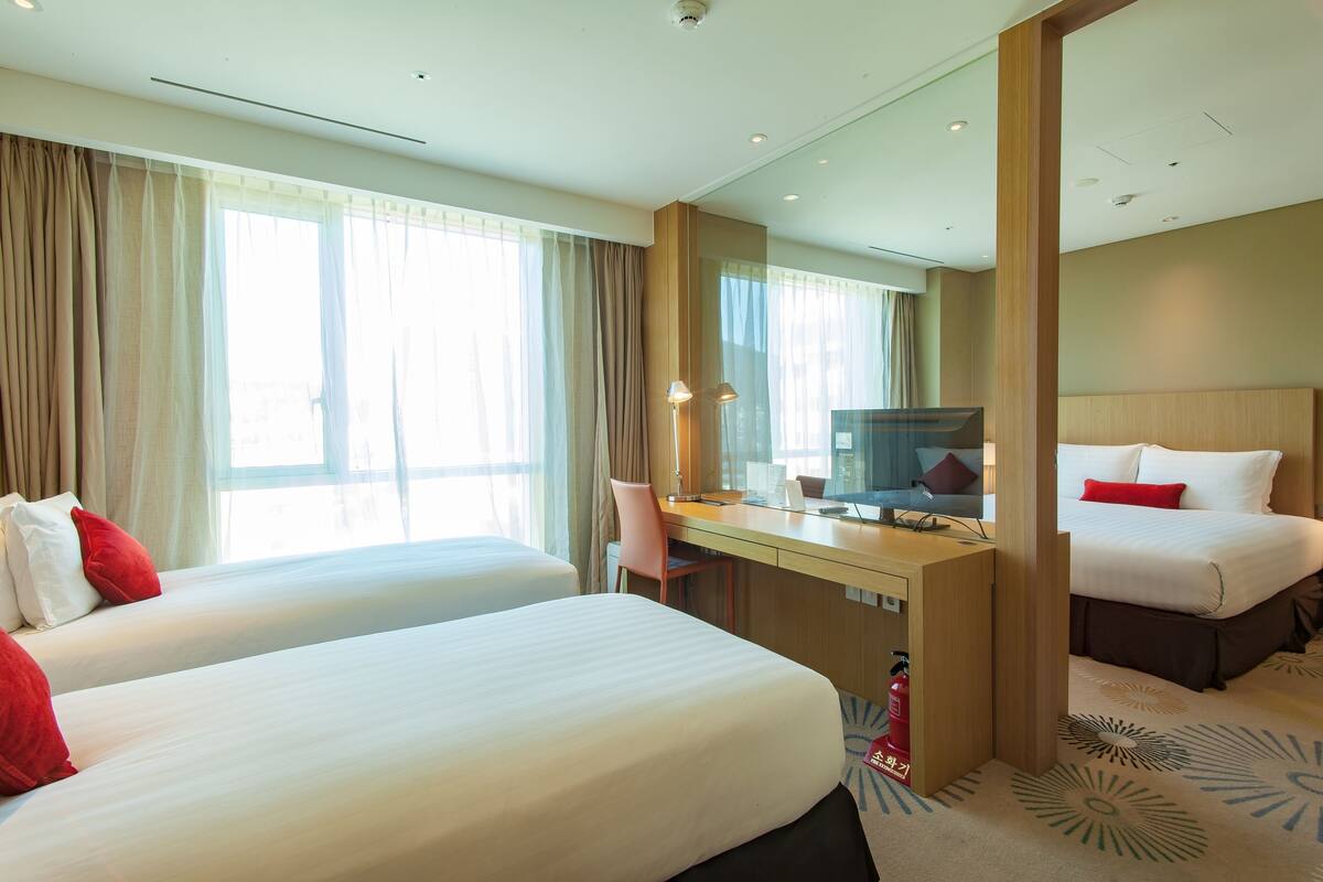 A hotel room with two beds, a desk, a chair, a television, and a large mirror.