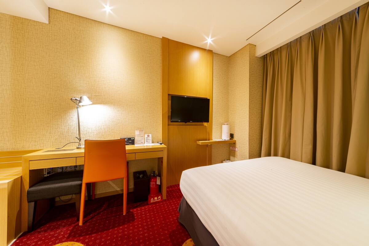 A hotel room with a bed, desk, chair, TV, and curtains.
