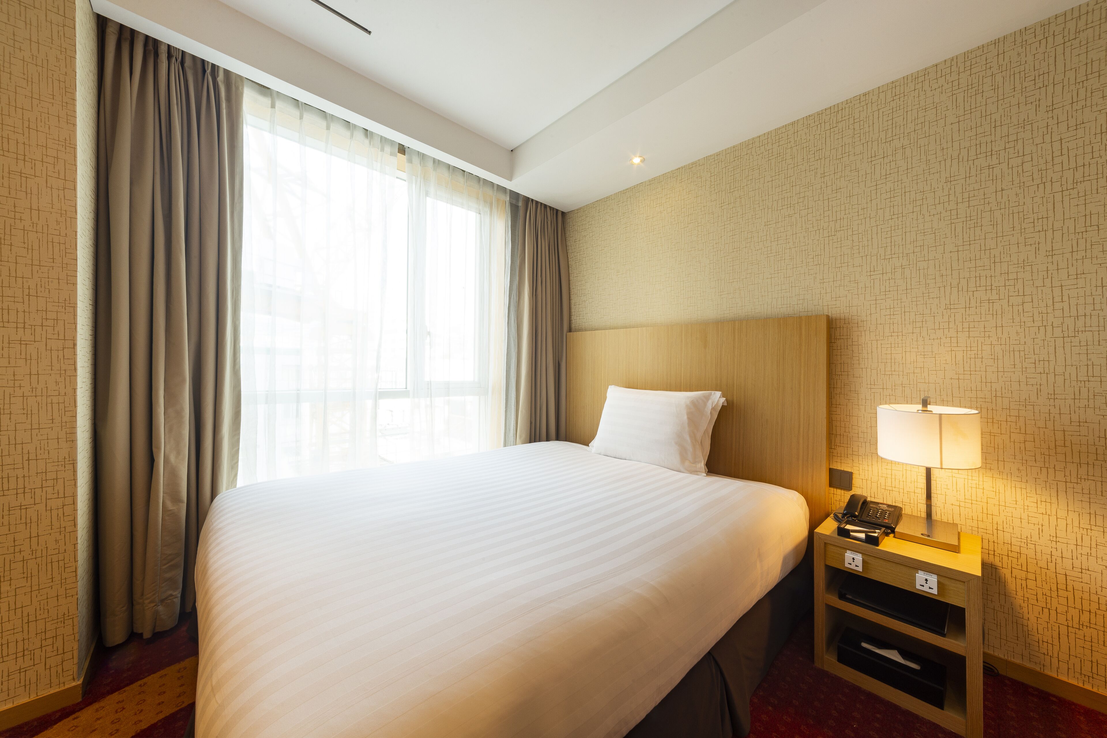 Ein Hotelzimmer mit einem großen Bett, einem Nachttisch mit Lampe und einer Wand mit Muster.