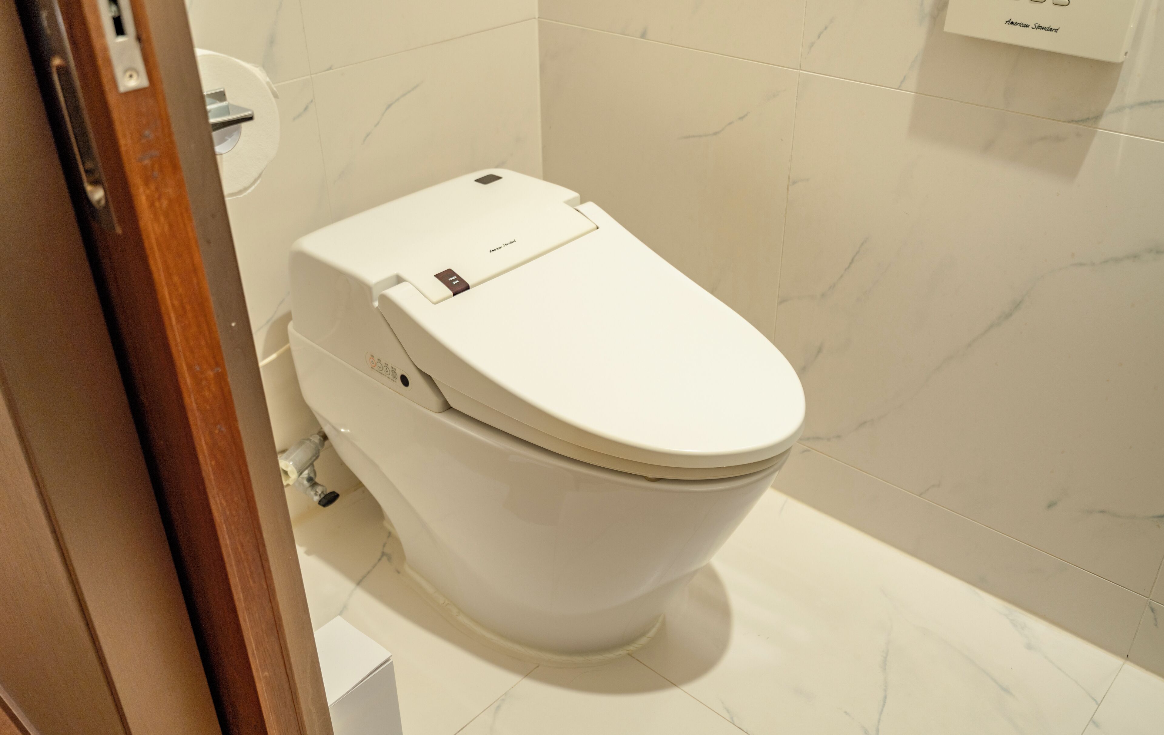 Un baño moderno con inodoro blanco, azulejos de mármol y un marco de puerta de madera.