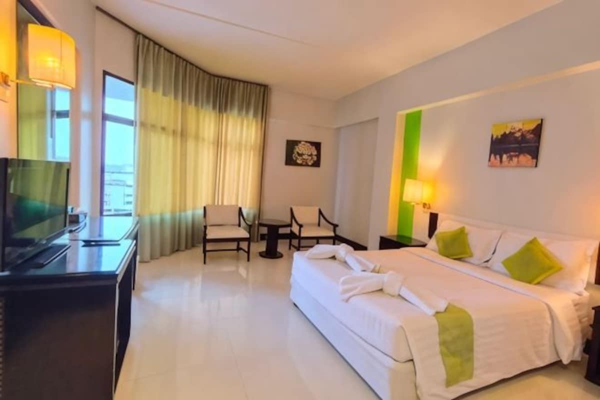 Habitación de hotel con cama, escritorio con televisor, dos sillas, mesita de noche y ventana con cortinas.