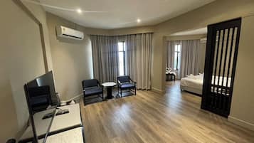 A hotel room with a desk, two chairs, a bed, and a TV.