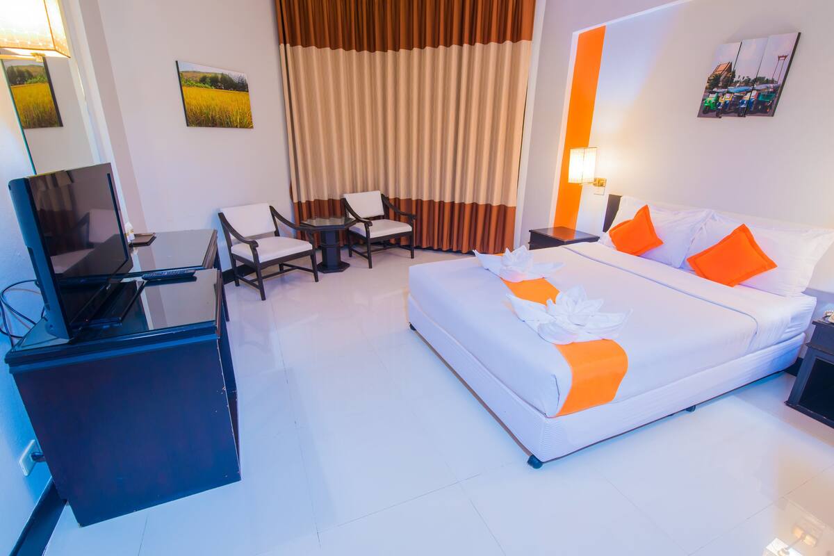 Una habitación de hotel con cama, dos sillas, un escritorio con computadora y televisor.