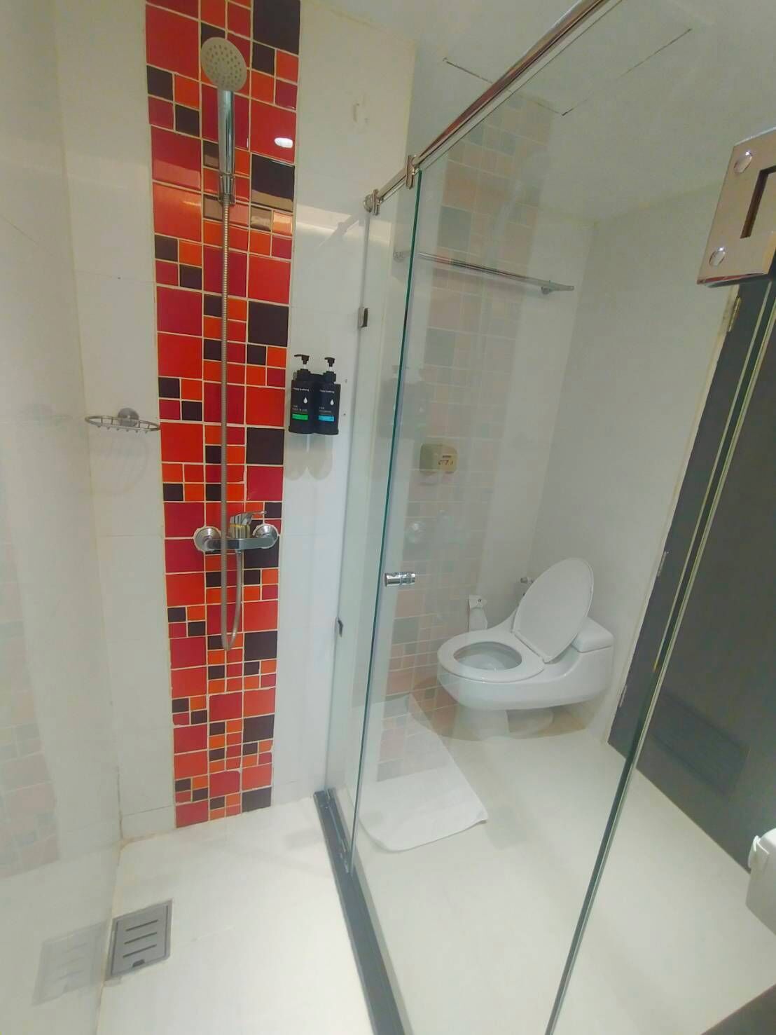 A modern bathroom with a glass-enclosed shower, a white toilet, and a tiled wall with red and black accents.
