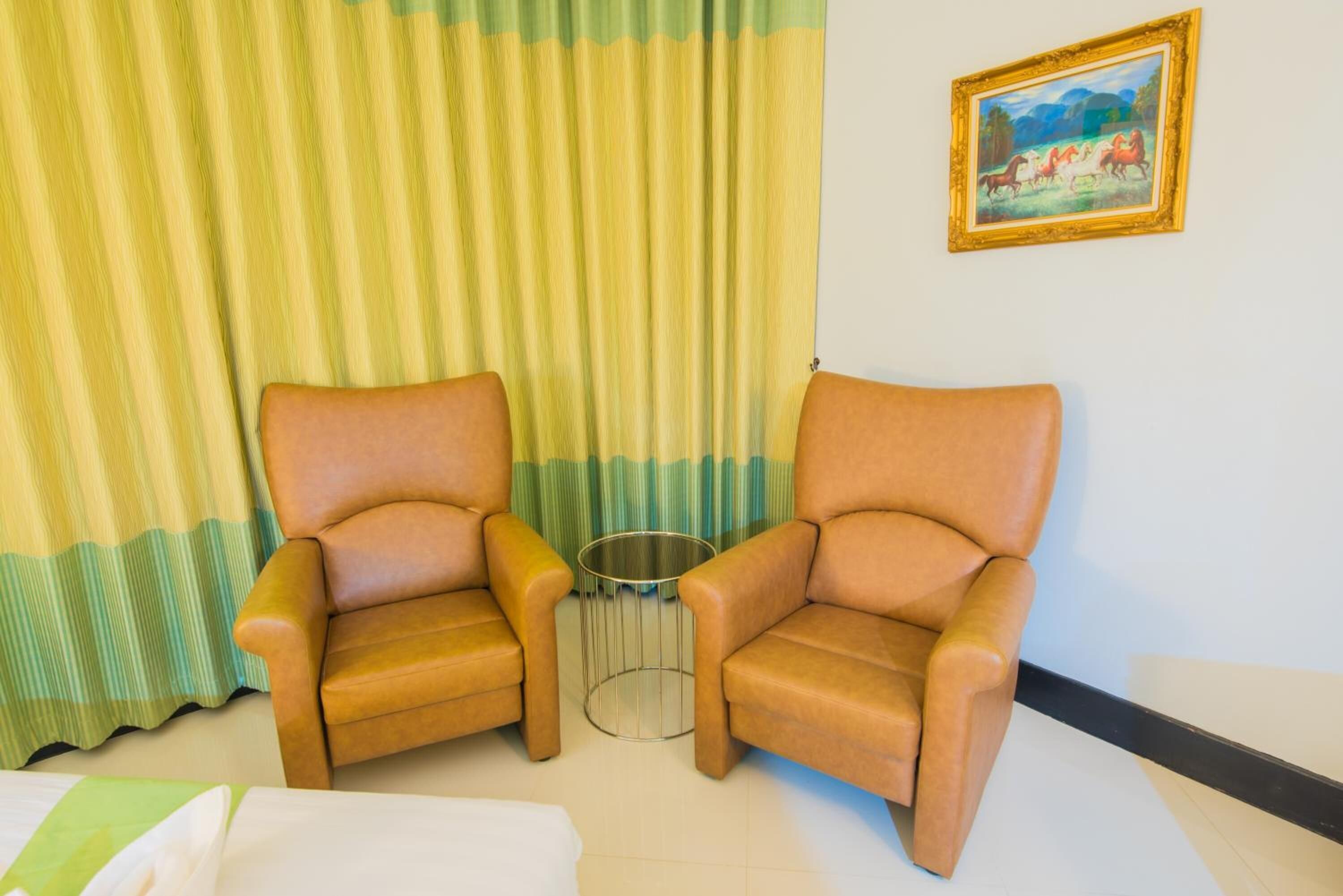 A room with two brown leather armchairs, a small metal table, a green and yellow striped curtain, and a framed painting on the wall.