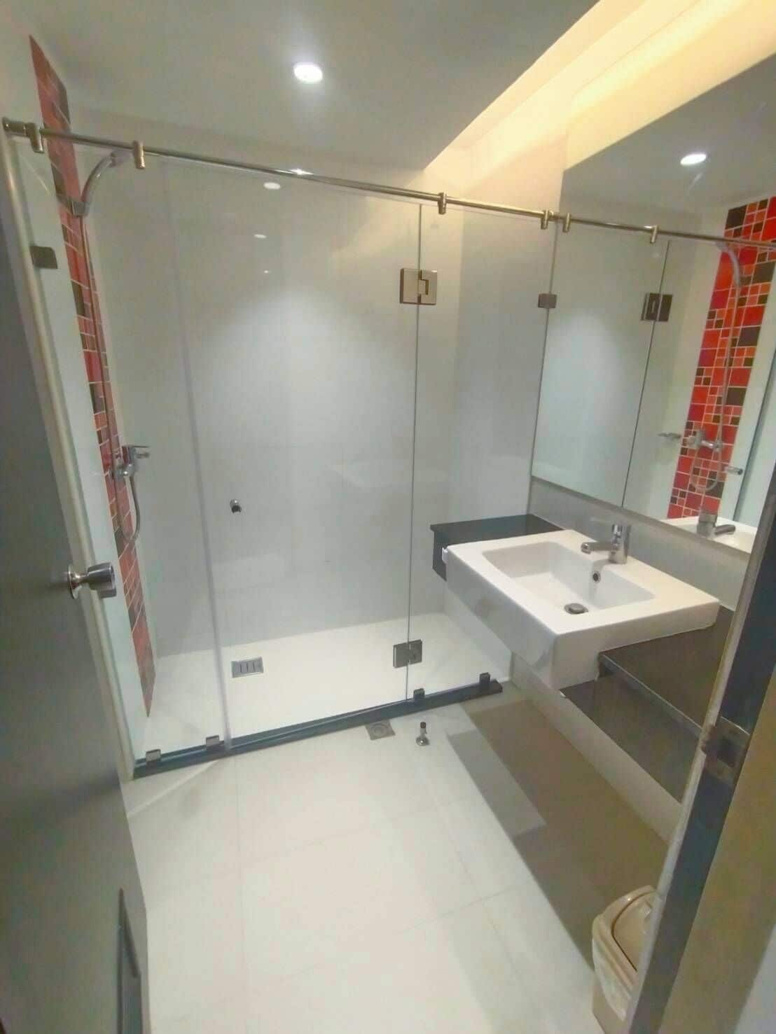 Un baño moderno con ducha envuelta en vidrio, un lavamanos blanco y un espejo grande.