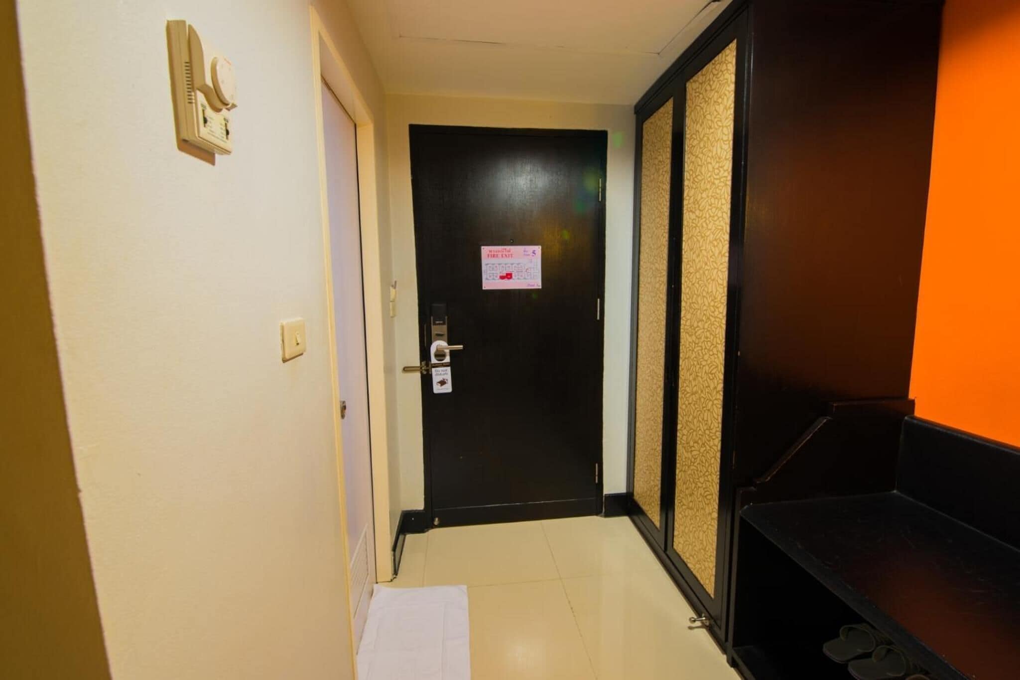 A hallway with a black door, a white towel on the floor, and a shoe rack.