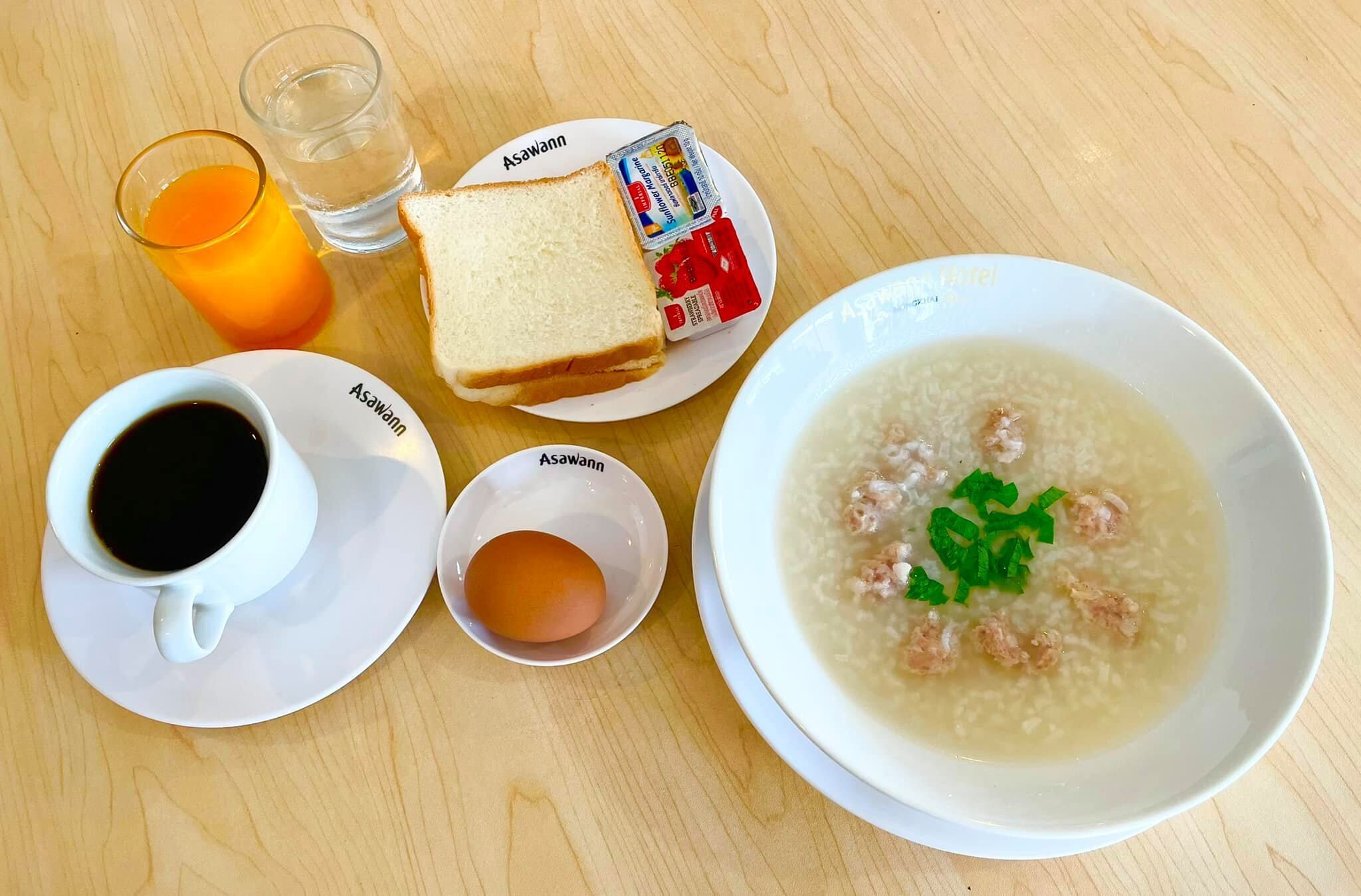 Un desayuno con un tazón de sopa, una taza de café, un vaso de jugo de naranja, una rebanada de pan y un cartón de leche sobre una mesa de madera.