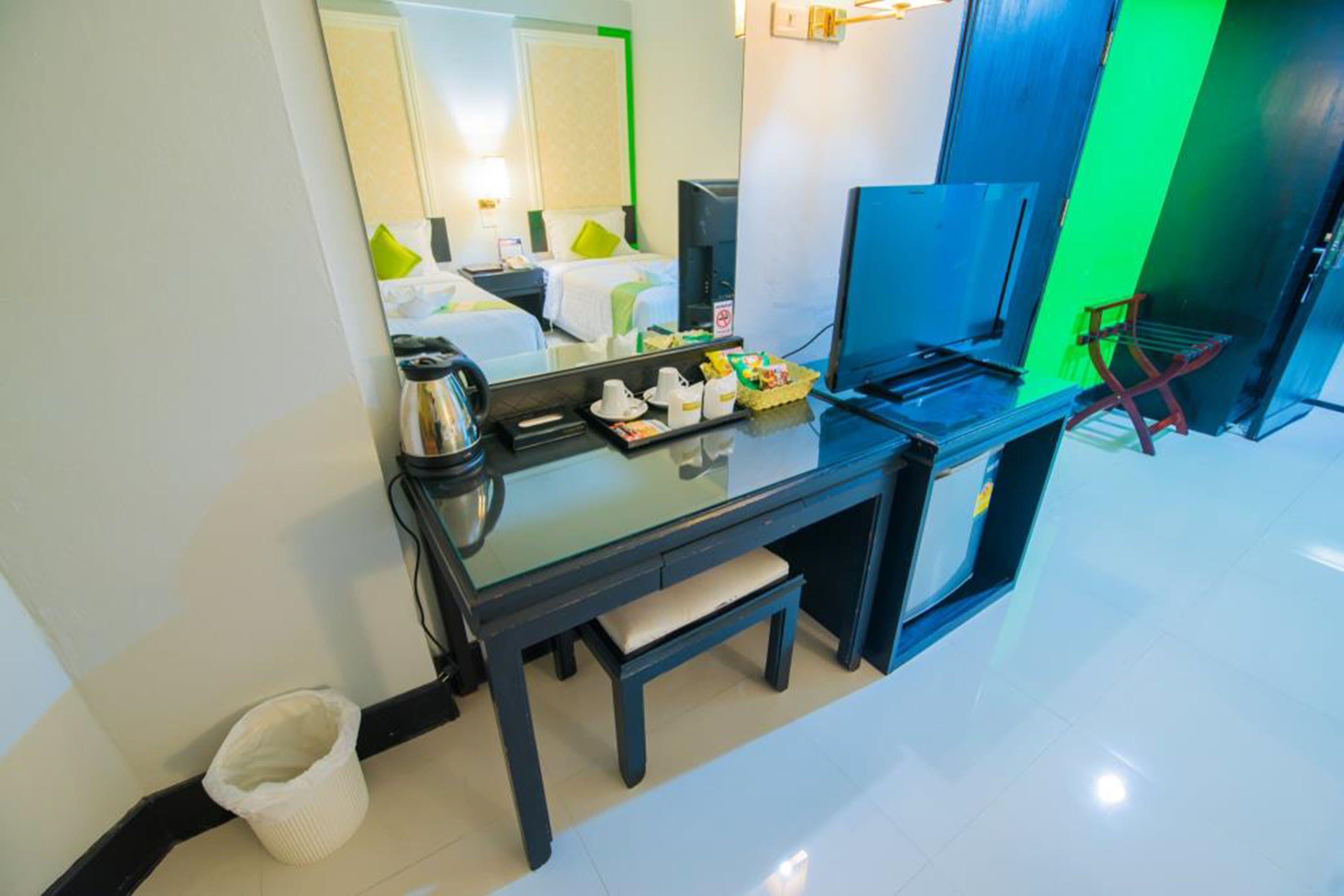 A hotel room with a glass desk, a chair, a television, and a bed with green pillows.