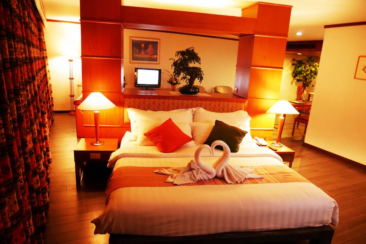 A well-lit hotel room with a large bed, two bedside lamps, a television, and a potted plant.