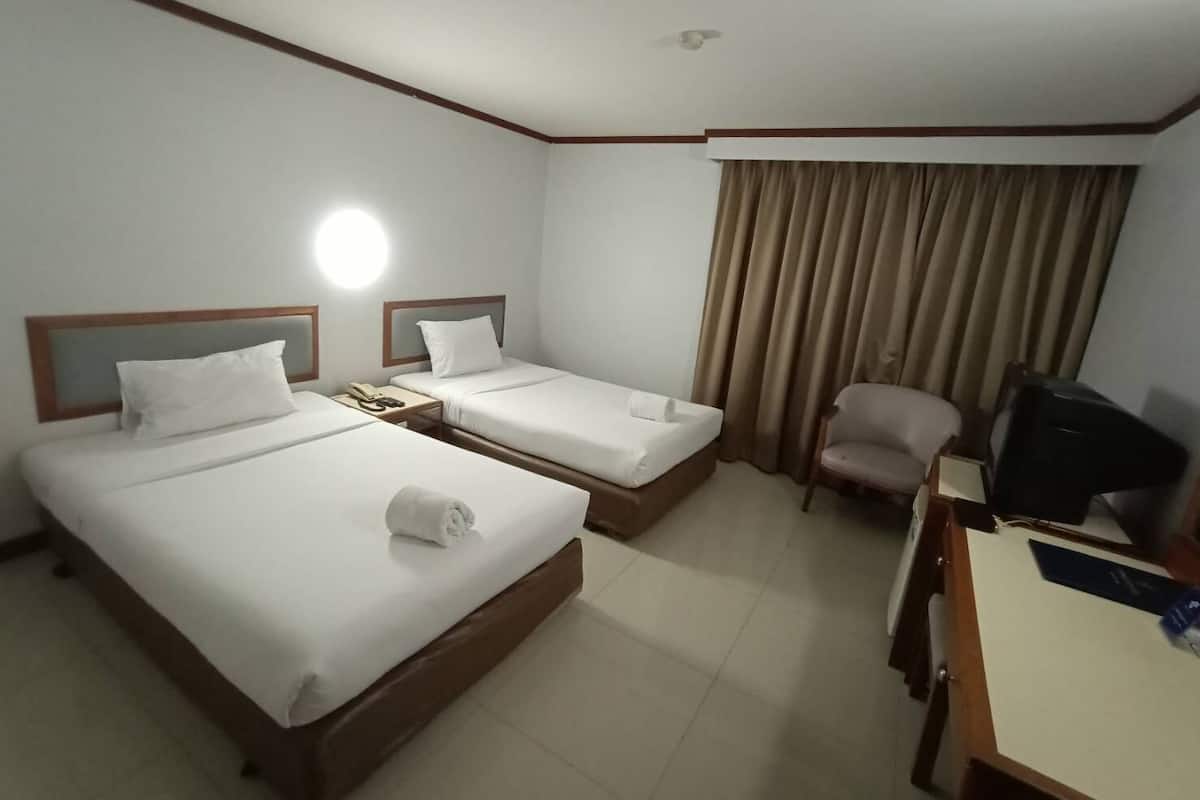 A hotel room with two beds, a desk, a chair, a television, and a window with curtains.