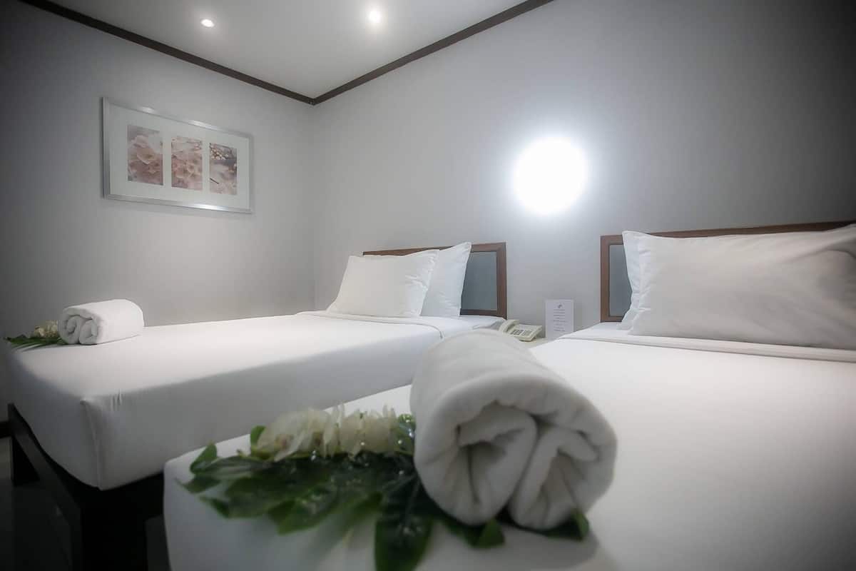 A hotel room with two beds, white linens, a telephone, and a framed picture on the wall.