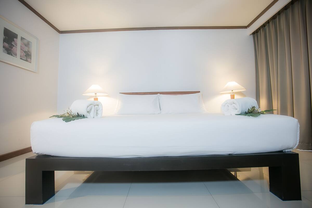 A large bed with white linens, two bedside lamps, and a dark bench.