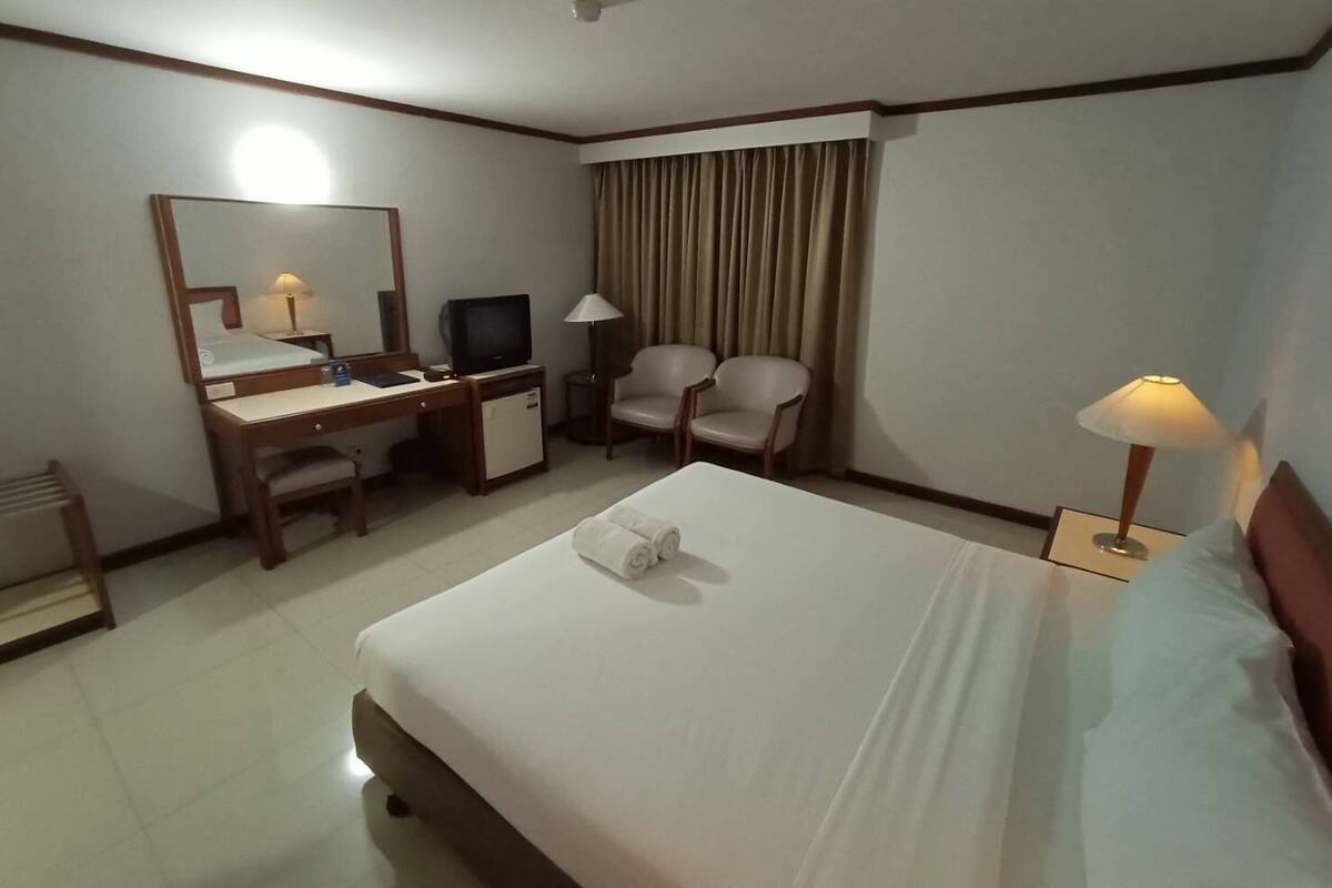 A hotel room with a bed, a desk with a computer, two chairs, a mirror, and a lamp.