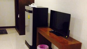 A small room with a wooden table, a television, a refrigerator, and a pink laundry basket. - Room Riverside (Chiang Mai)