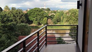A balcony with a metal railing, a tiled floor, and a view of a river and trees. - Room Riverside (Chiang Mai)