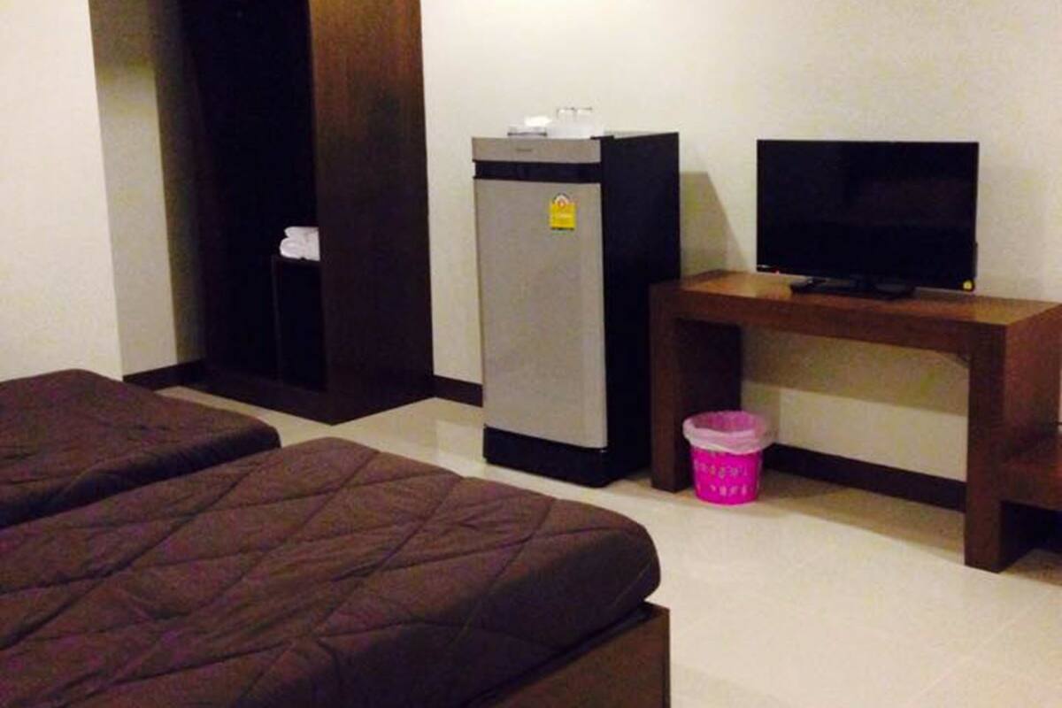 A hotel room with two beds, a desk with a television, a refrigerator, and a trash bin.