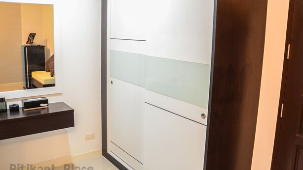 A modern bathroom with a mirror, a dark countertop, and a white door with a glass panel. - Pitikant Place (Lam Luk Ka)