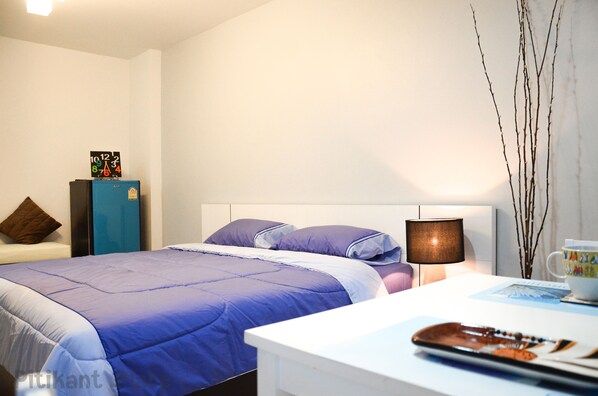A hotel room with a bed, a nightstand, a lamp, and a wall clock. - Pitikant Place (Lam Luk Ka)