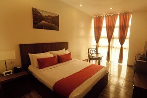 Habitación de hotel con una cama grande, una mesita de noche con lámpara, una silla y un escritorio.