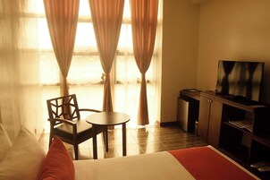 Una habitación de hotel con cama, televisión, una mesita, una silla y cortinas.