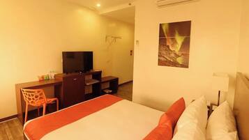 A hotel room with a bed, a desk, a chair, a television, and a wall-mounted air conditioner.