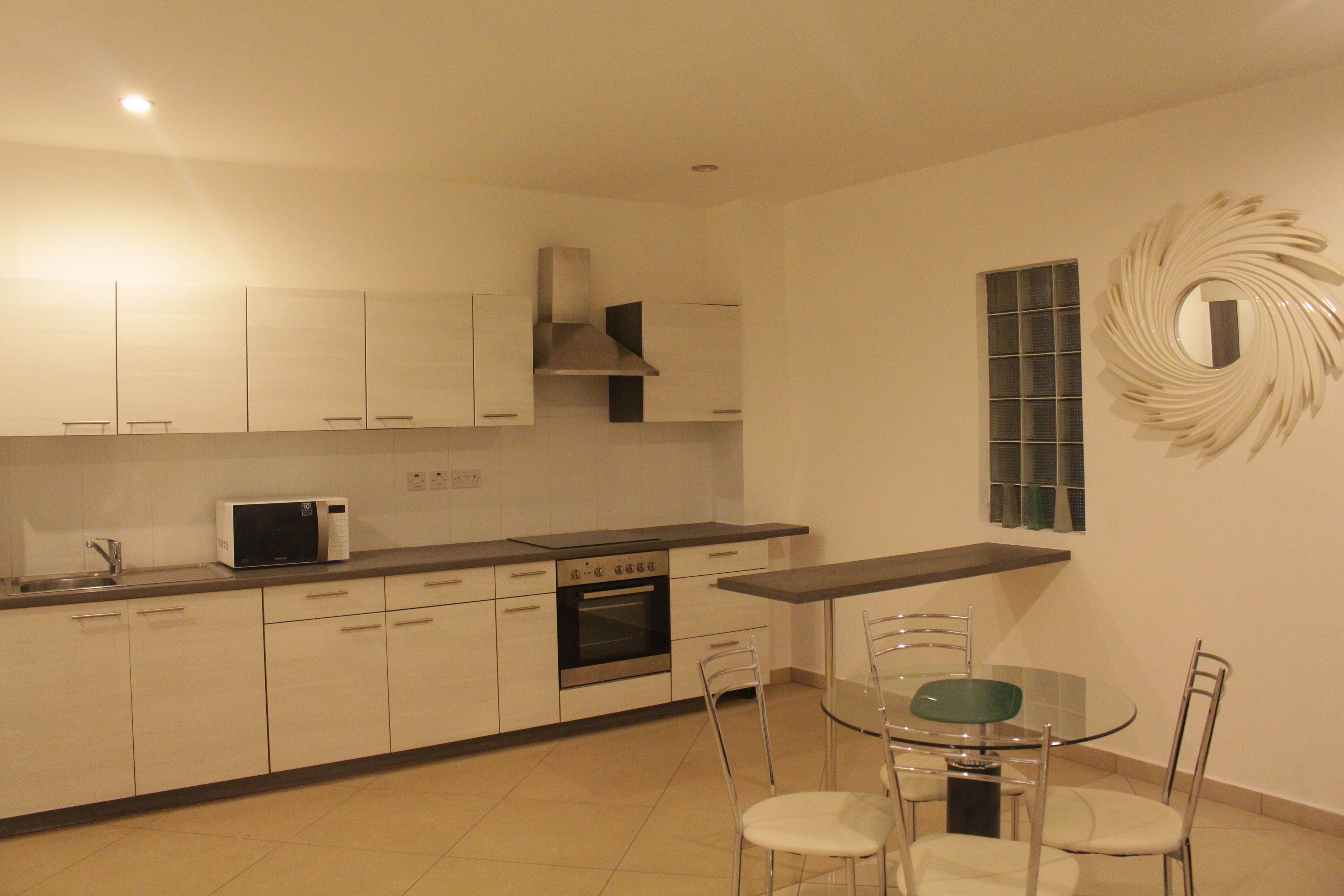 A modern kitchen with white cabinets, a microwave, an oven, and a dining table with chairs.