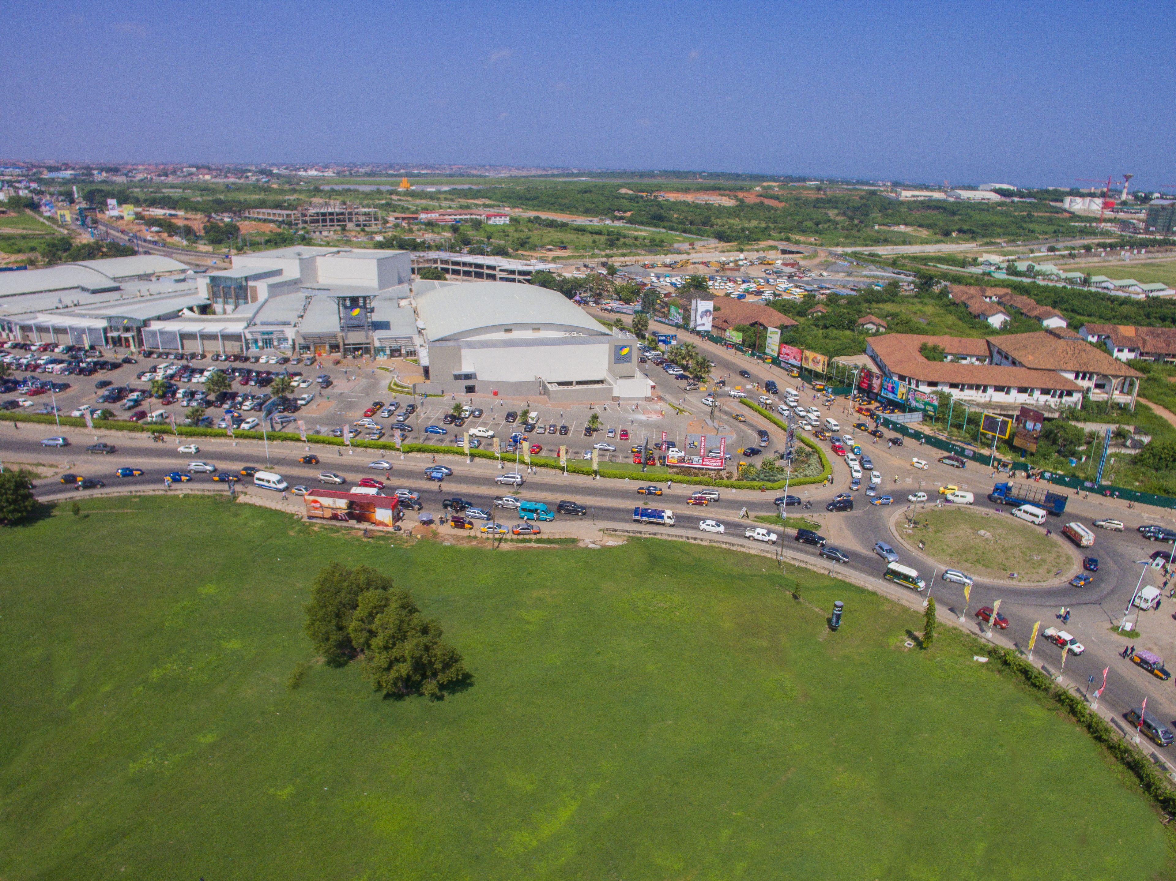 An aerial view of a commercial area with a large building, parking lots, and a roundabout.