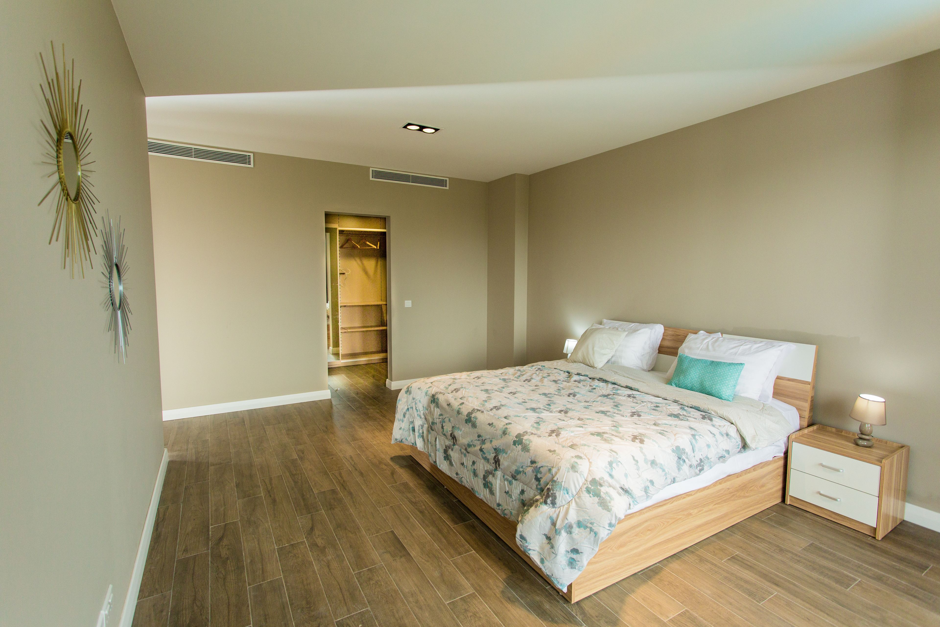 Une chambre avec un lit en bois, une table de chevet, une armoire et une bouche d’aération au plafond.