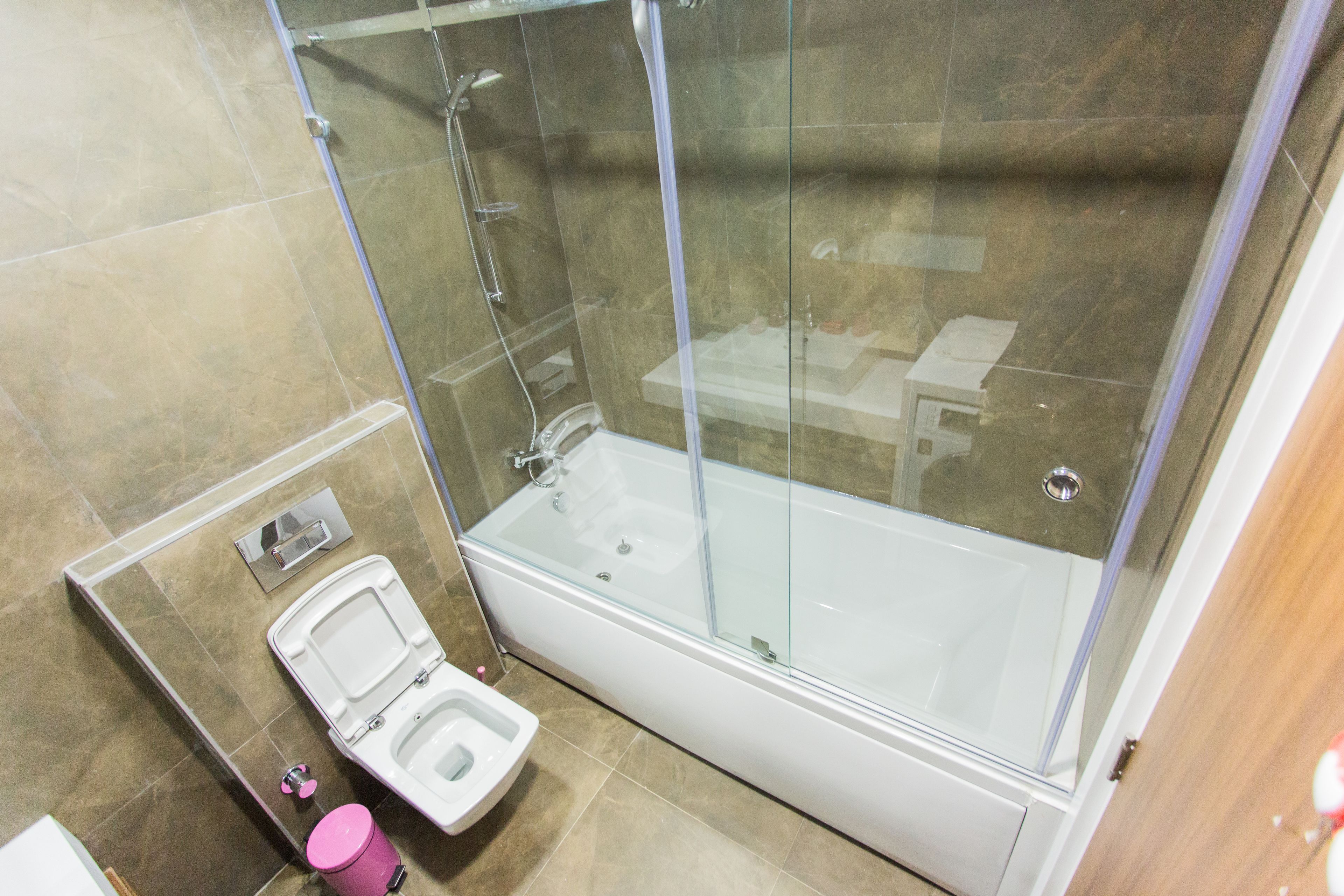 Et moderne badeværelse med en glasafskærmet brusekabine, et hvidt badekar og et separat toiletområde.